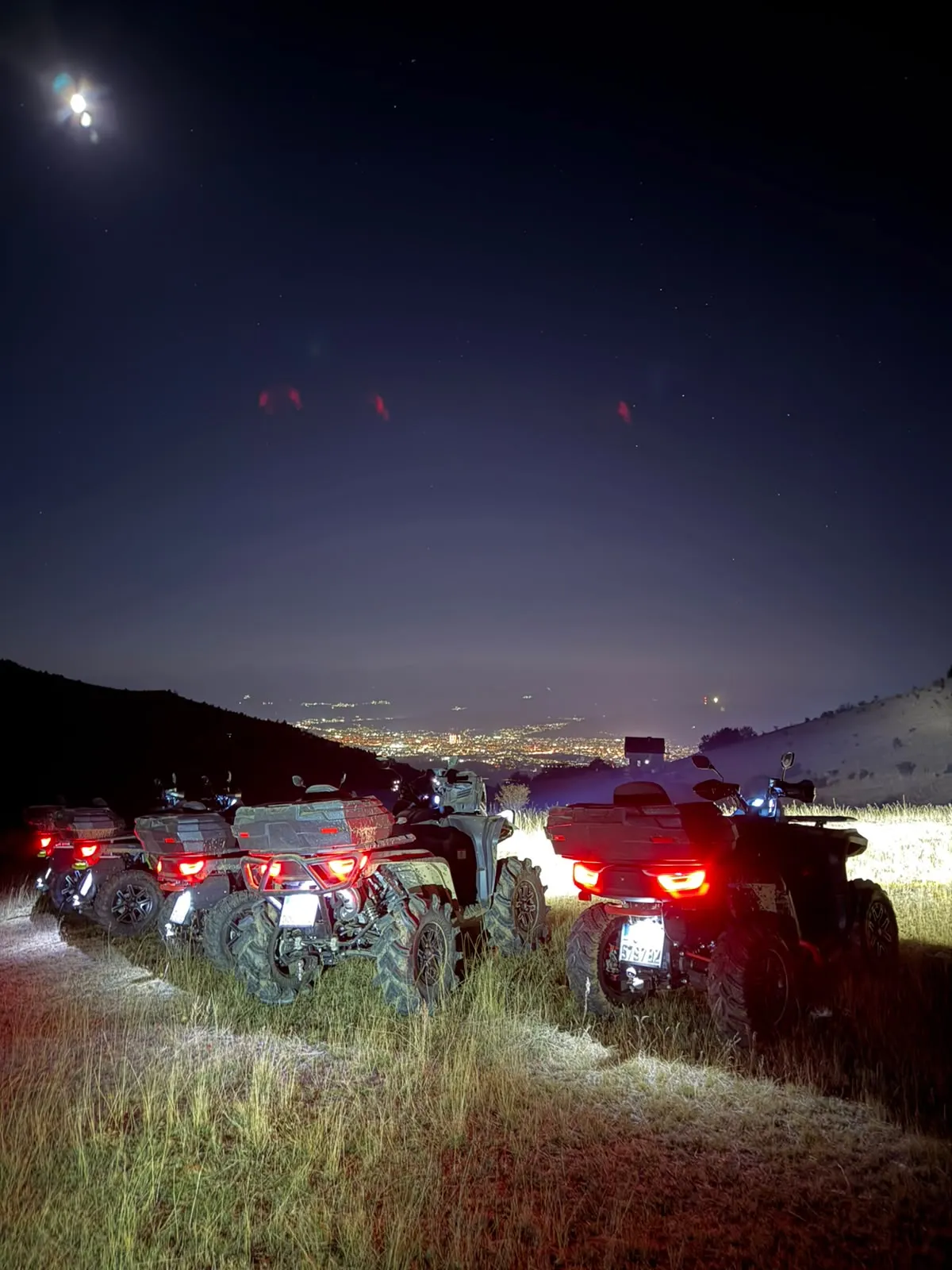 Quad bikes with headlights on, parked on a hill above Skopje’s city lights at night